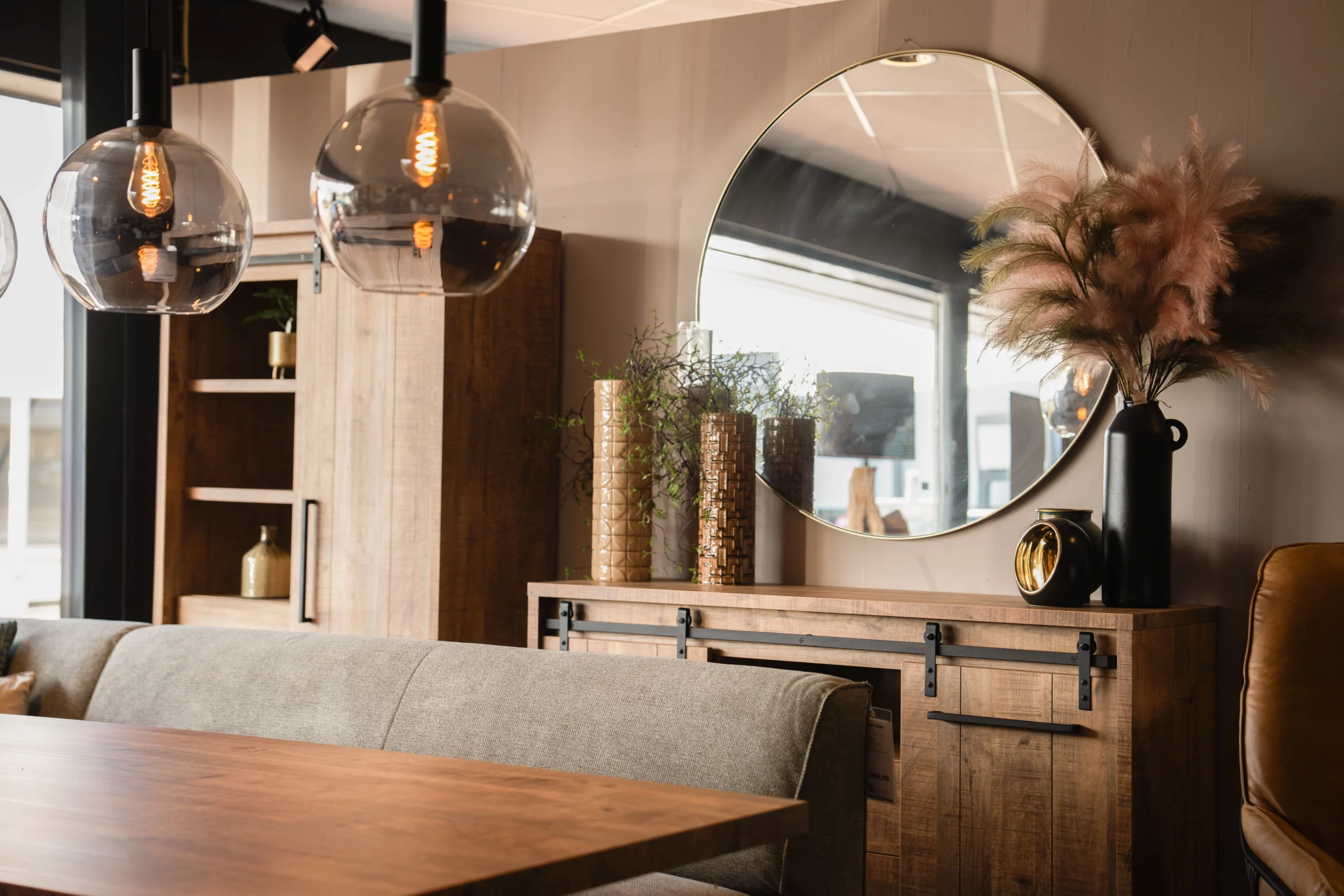 Grote ronde spiegel boven een industriële dressoir en naast een wandkast