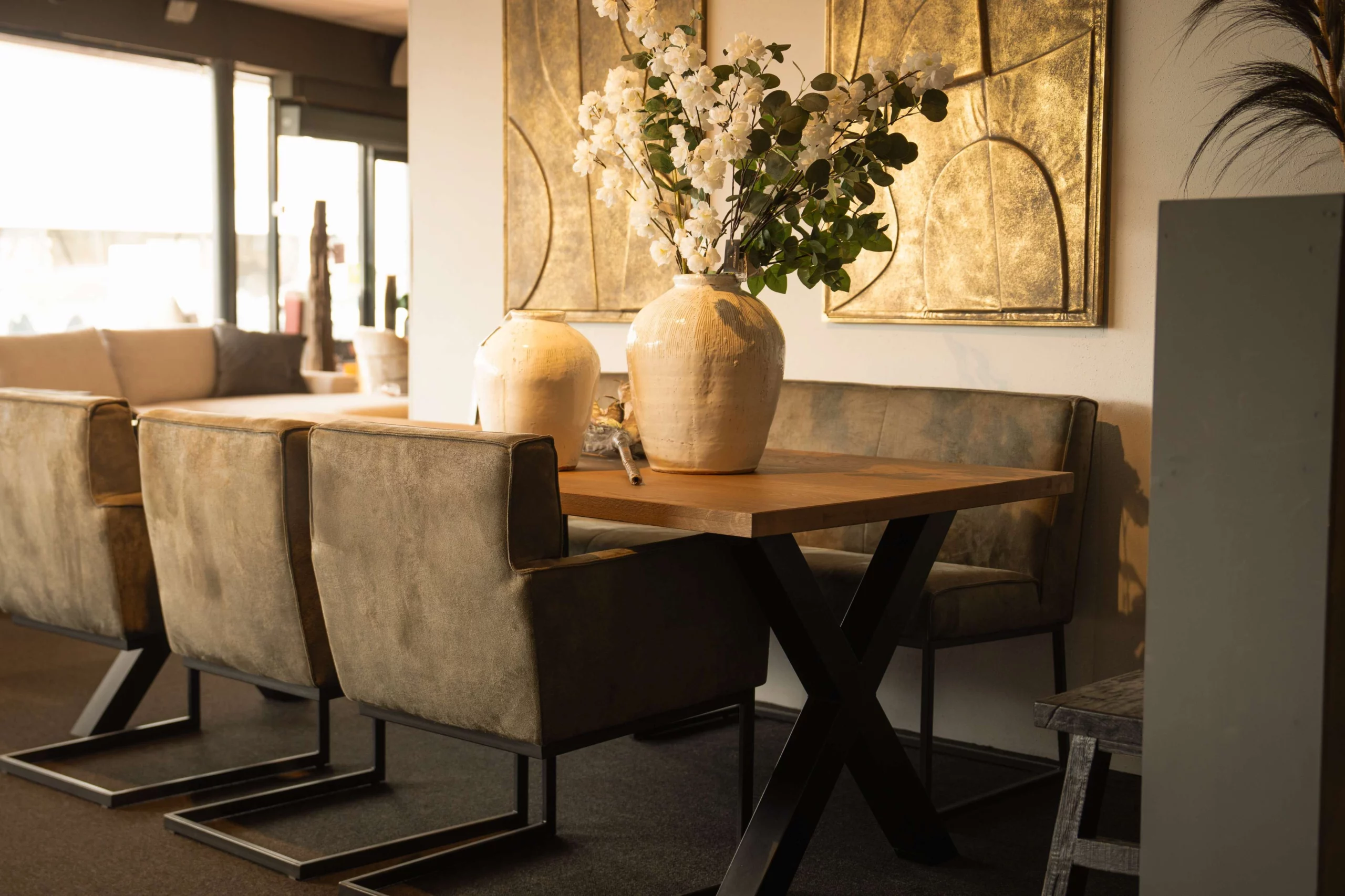 Grote vitte vaas op een houten eettafel met kruispoot, grijze eetkamerstoelen en eetkamerbank